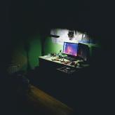 Two computer screens on a desk in a dark room. The light is focused on the computers