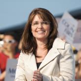 Sarah Palin in a white jacket, in front of a crowd, smiling.