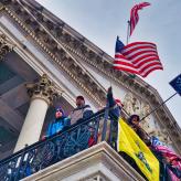 A U.S Flag, A Trump and Pence flag and other flags flying from the balcony of the Capitol building.